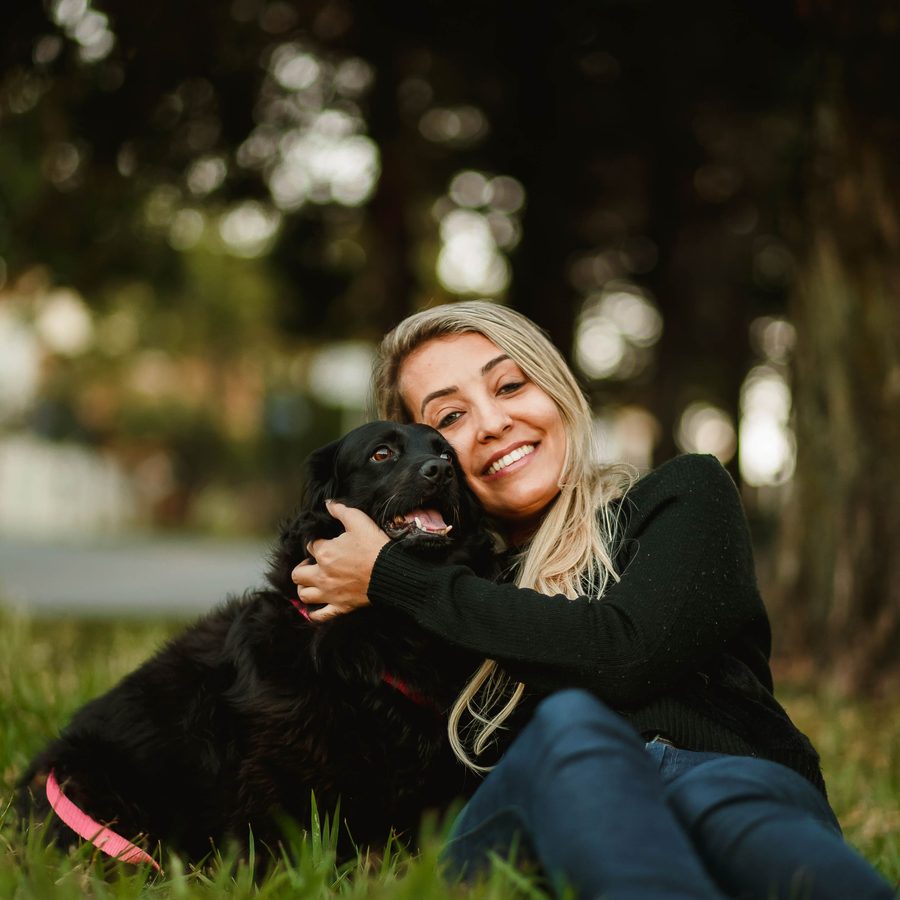 A woman hugging her black dog in the grass